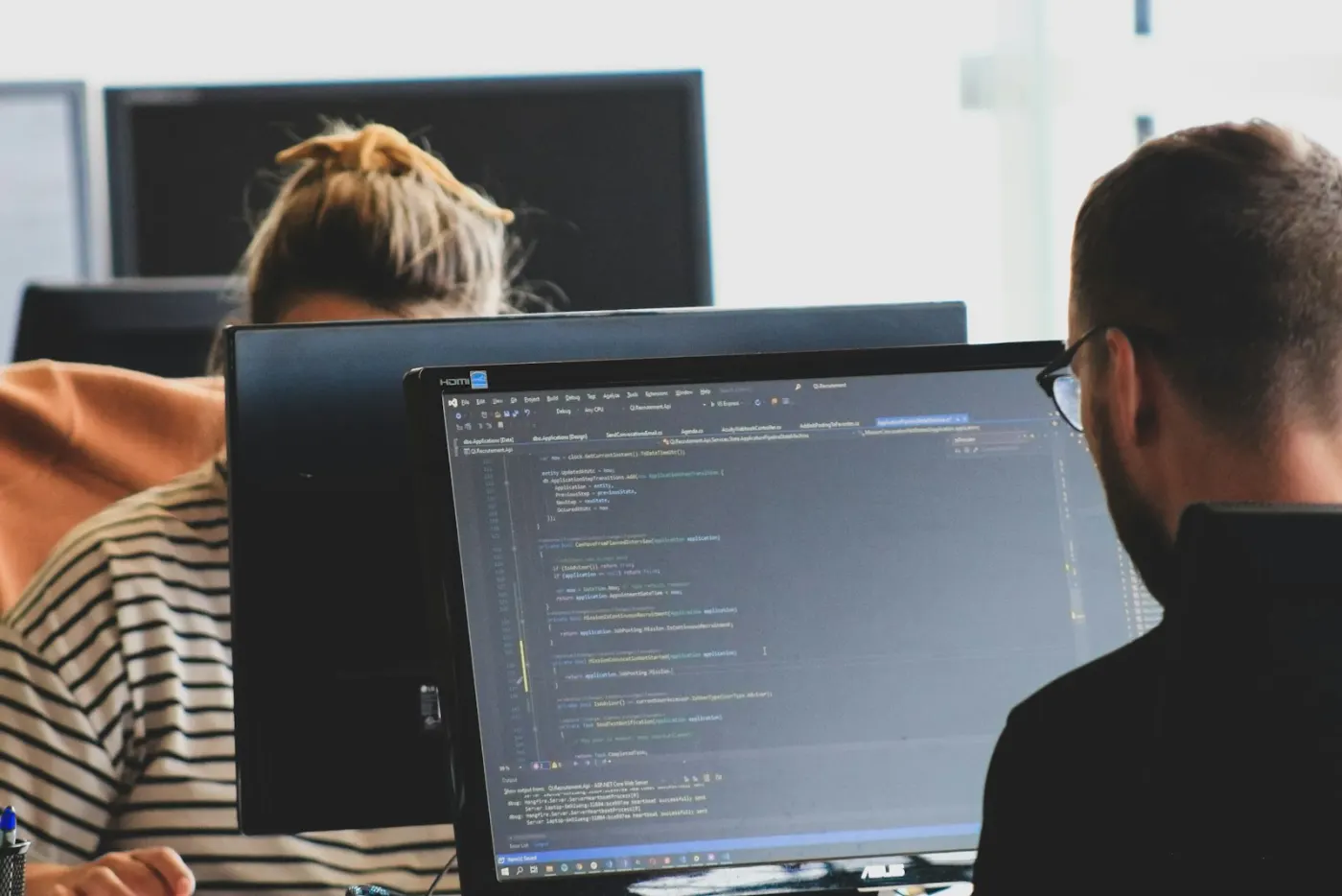 Two engineers working on code across several monitors